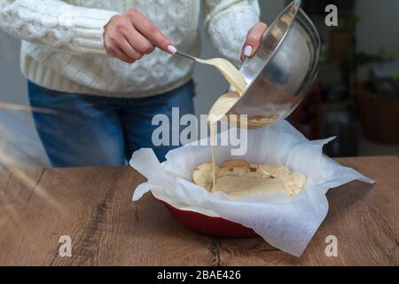 La hostess prepara la mela charlotte a casa in cucina e versa l'impasto in un piatto da forno. Pasta di mele crude Foto Stock