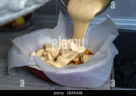 La hostess prepara la mela charlotte a casa in cucina e versa l'impasto in un piatto da forno. Pasta di mele crude Foto Stock