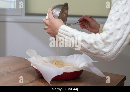 La hostess prepara la mela charlotte a casa in cucina e versa l'impasto in un piatto da forno. Pasta di mele crude Foto Stock