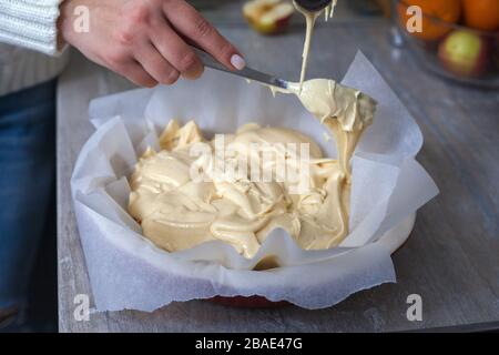 La hostess prepara la mela charlotte a casa in cucina e versa l'impasto in un piatto da forno. Pasta di mele crude Foto Stock