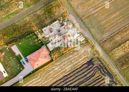 Vista aerea dall'alto di due case private, una in costruzione con fondament in cemento e pareti in mattoni e un'altra rifinita con tetto di tegole rosse. Foto Stock