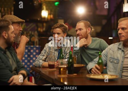 Gruppo di amici seduti al tavolo che parlano l'uno con l'altro e bevono birra che si incontrano al bar Foto Stock