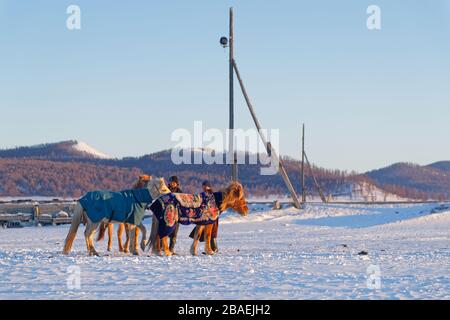 KHATGAL, MONGOLIA, 27 febbraio 2020 : giovani piloti sono venuti a bere i loro cavalli in un buco scavato nel lago. Foto Stock