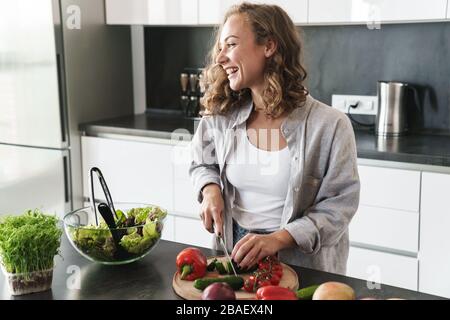 Giovane donna felice che fa un'insalata in cucina, tagliando le verdure Foto Stock