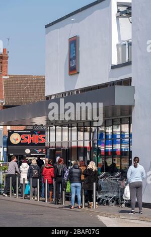 Gli acquirenti si accodano al di fuori del superstore di Aldi a Westcliff on Sea durante il blocco per l'epidemia di virus pandemico del Coronavirus COVID-19. Alcuni si avvicinano Foto Stock