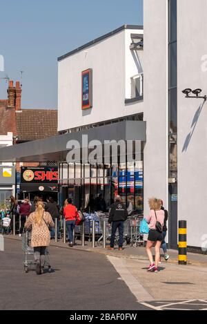 Gli acquirenti si accodano al di fuori del superstore di Aldi a Westcliff on Sea durante il blocco per l'epidemia di virus pandemico del Coronavirus COVID-19. Alcuni si avvicinano Foto Stock