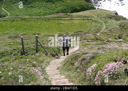 Lone Man Hiker camminare giù i gradini di legno alla bocca di Marsland sul percorso costiero del sud-ovest, Devon del Nord, Inghilterra, Regno Unito Foto Stock