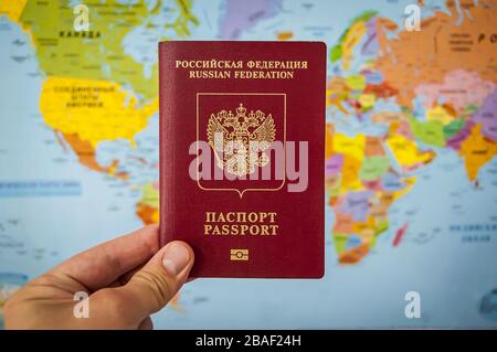 Mano che tiene il passaporto della Russia contro il colorato atlante della mappa del mondo. Concetto di passaporto russo, concetto di viaggio per turisti russi. Foto Stock