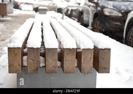 una panchina in legno sotto la prima neve sulla strada Foto Stock