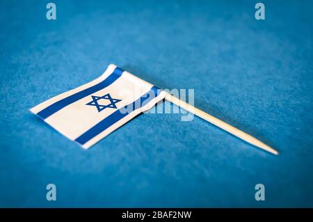 Una piccola bandiera di Israele su uno stuzzicadenti di legno su uno sfondo di carta blu, immagine closeup. Bella immagine del concetto di bandiera israeliana Foto Stock