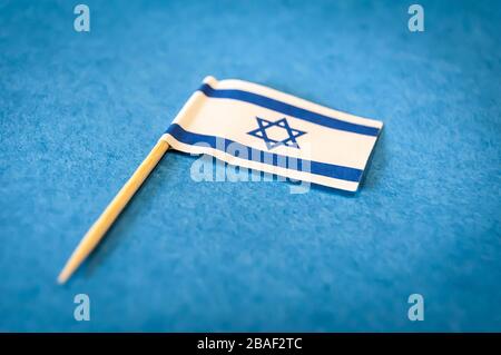 Una piccola bandiera di Israele su uno stuzzicadenti di legno su uno sfondo di carta blu, immagine closeup. Bella immagine del concetto di bandiera israeliana Foto Stock