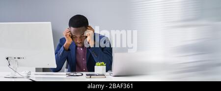 Un giovane uomo d'affari preoccupato che guarda il computer alla scrivania dell'ufficio Foto Stock