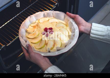 La padrona di casa prepara la mela charlotte in cucina e mette in forno una torta di mele, in un piatto da forno. Pasta di mele cruda Foto Stock