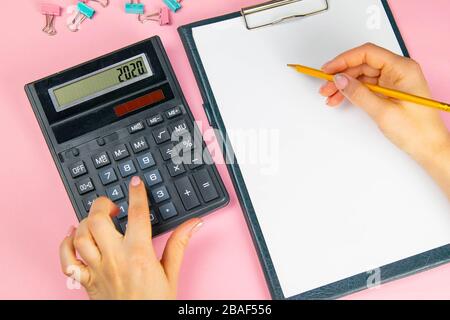 Le mani di una donna contano su una calcolatrice e scrivono note. Vista dall'alto delle mani della donna d'affari sul foglio bianco. Concetto di finanza e business Foto Stock