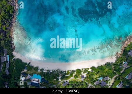 Vista aerea del resort sulla spiaggia tropicale con baia turchese e lussureggiante collina, Anse Petite, Mahe Island, Seychelles Foto Stock