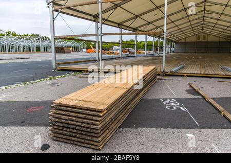 Costruzione di stand di una fiera regionale, costruzione di tende, pali di legno e tavole di legno per il pavimento della tenda sulla pila, tende sullo sfondo, alu Foto Stock