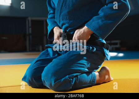 Giovane combattente caucasico judo in kimono blu con cintura nera in posa fiduciosa in palestra, forte e sano. Pratica arti marziali capacità di combattimento. Superare, raggiungere l'obiettivo, auto-costruire. Foto Stock