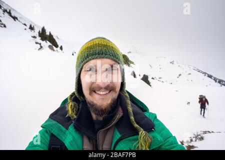 Ritratto Selfie felice uomo barbuto in giacca verde a montagne innevate Foto Stock
