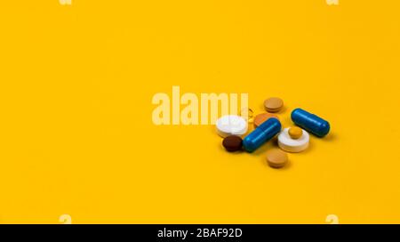 Multicolor compresse e pillole capsule da flacone di vetro su sfondo giallo Salute attenzione primo piano banner orizzontale Copia spazio. Coronavirus covid-19 c Foto Stock