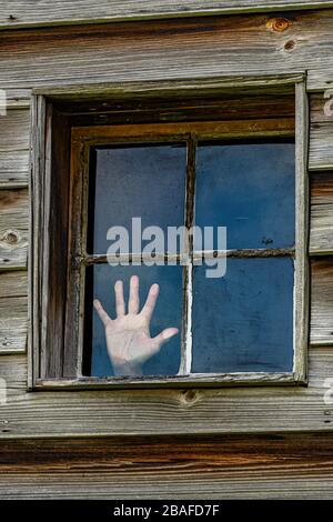 Colpo verticale di una finestra a quattro pannelli in un muro di legno con una mano di una donna premuta contro un pannello come se provasse a fuggire. Foto Stock