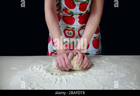 Le mani della donna impastano l'impasto con il Flour bianco sul tavolo da cucina su sfondo scuro. Foto Stock