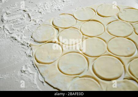 Pasta arrotolata cruda tagliata a tondi con farina su tavola bianca. Processo di cottura gnocchi. Foto Stock