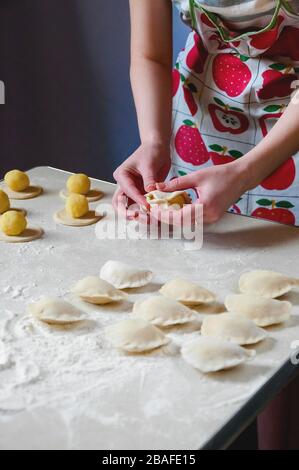 Donna mani sculture gnocchi con patate su sfondo bianco. Cibo ucraino tradizionale. Foto Stock