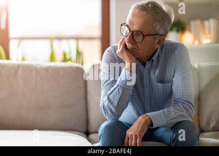 Preoccupato uomo anziano seduto da solo nella sua casa Foto Stock