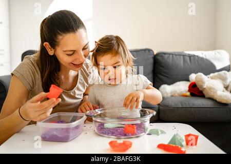 Madre giovane con bambino che gioca sabbia cinetica. Buon tempo di Unione insieme. Sviluppo della creatività Foto Stock