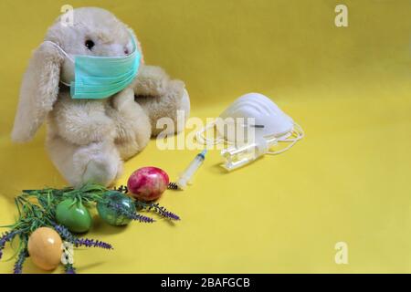 Pasqua durante il concetto di coronavirus. Bunny , uova e maschera su sfondo giallo. COVID-19 focolaio, celebrazione e soggiorno concetto di casa. Copia spazio Foto Stock