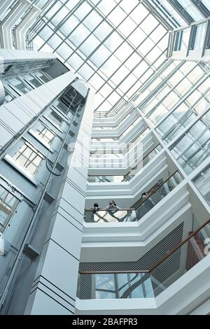 Sotto la vista di diversi uomini d'affari che discutono dei punti di lavoro mentre si trovano su uno dei balconi all'interno di un grande centro uffici Foto Stock