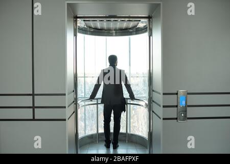 Vista posteriore del giovane ed elegante uomo d'affari in formalwear in piedi in ascensore con porta aperta mentre godendo la pausa nel centro d'ufficio Foto Stock