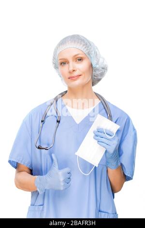 Giovane dentista, chirurgo o altro professionista che punta la maschera protettiva nella sua mano con i guanti mentre altamente raccomanda di indossarla Foto Stock