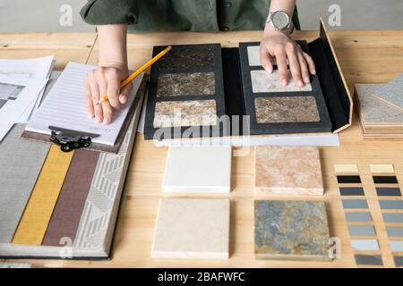 Mani di giovane donna che prende appunti su carta mentre sceglie campione di pannello dalla raccolta durante il lavoro su nuovo ordine Foto Stock