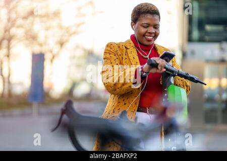 Giovane donna con scooter elettrico che controlla il suo smartphone Foto Stock