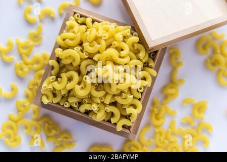 Concetto di cucina italiana e design del menu. Pasta gialla non cotta in scatola di legno su sfondo bianco. Disposizione piatta. Vista dall'alto. Foto Stock