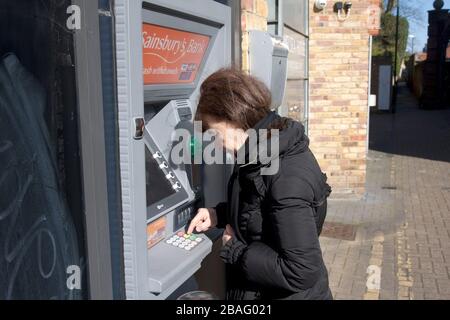 Donna di mezza età durante il coronavirus 2020 a pressione ATM tastiere Foto Stock