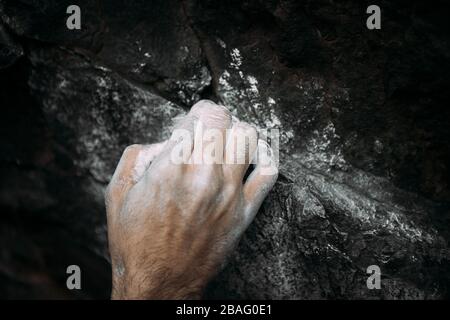 Primo piano di una mano di scalatore di roccia ricoperta di gesso mentre si crema e si poteri per salire su un masso di roccia Foto Stock