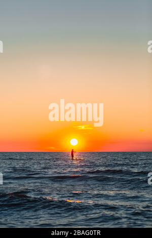 La silhouette di un uomo paddle imbarco durante il tramonto a un'ora d'oro sulle acque blu del lago Michigan Foto Stock