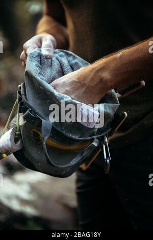 Primo piano della mano di un scalatore di roccia che si prepara a salire su un masso di roccia con le mani nella sua borsa di gesso Foto Stock