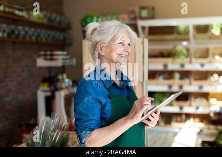 Donna senior che lavora in un piccolo negozio di alimentari Foto Stock