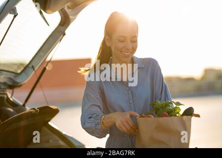 Giovane donna nel parcheggio, carico shopping in stivale di auto Foto Stock