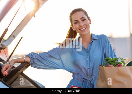 Giovane donna nel parcheggio, carico shopping in stivale di auto Foto Stock
