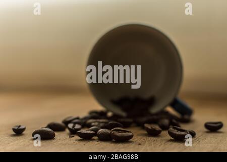 Chicchi di caffè su un tavolo di legno con una tazza sul fondo Foto Stock