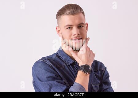 Primo piano di attraente hipster con la mano e sorridente, mentre isolato su sfondo bianco. Giovane e bell'uomo in abbigliamento casual Foto Stock