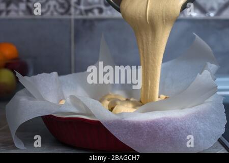 La hostess prepara la mela charlotte a casa in cucina e versa l'impasto in un piatto da forno. Pasta di mele crude Foto Stock