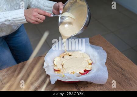 La hostess prepara la mela charlotte a casa in cucina e versa l'impasto in un piatto da forno. Pasta di mele crude Foto Stock