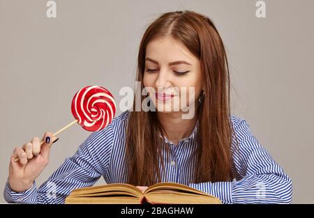 donna che legge libri a casa, lei gode anche caramelle deliziose Foto Stock