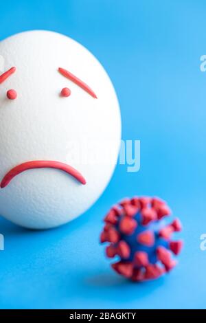 Modello di coronavirus plastificato e isolato di uovo su sfondo blu. Modello plastilina di coronavirus e uovo di pasqua raffigurante paura e tristezza. Grande Foto Stock