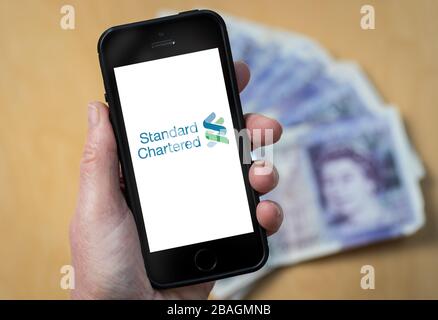 Una donna che guarda il logo Standard Chartered Bank su un telefono cellulare. (Solo per uso editoriale) Foto Stock